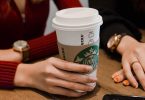 "An image of a Starbucks barista holding a cup of frappuccino with a straw and the text overlay of "How to Order a Healthier Starbucks Frappuccino: Tips and Tricks for Enjoying Your Favorite Treat with Less Guilt