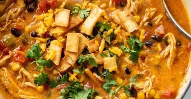 Steaming bowl of vibrant Crock Pot Tortilla Soup topped with fresh cilantro and shredded cheese.